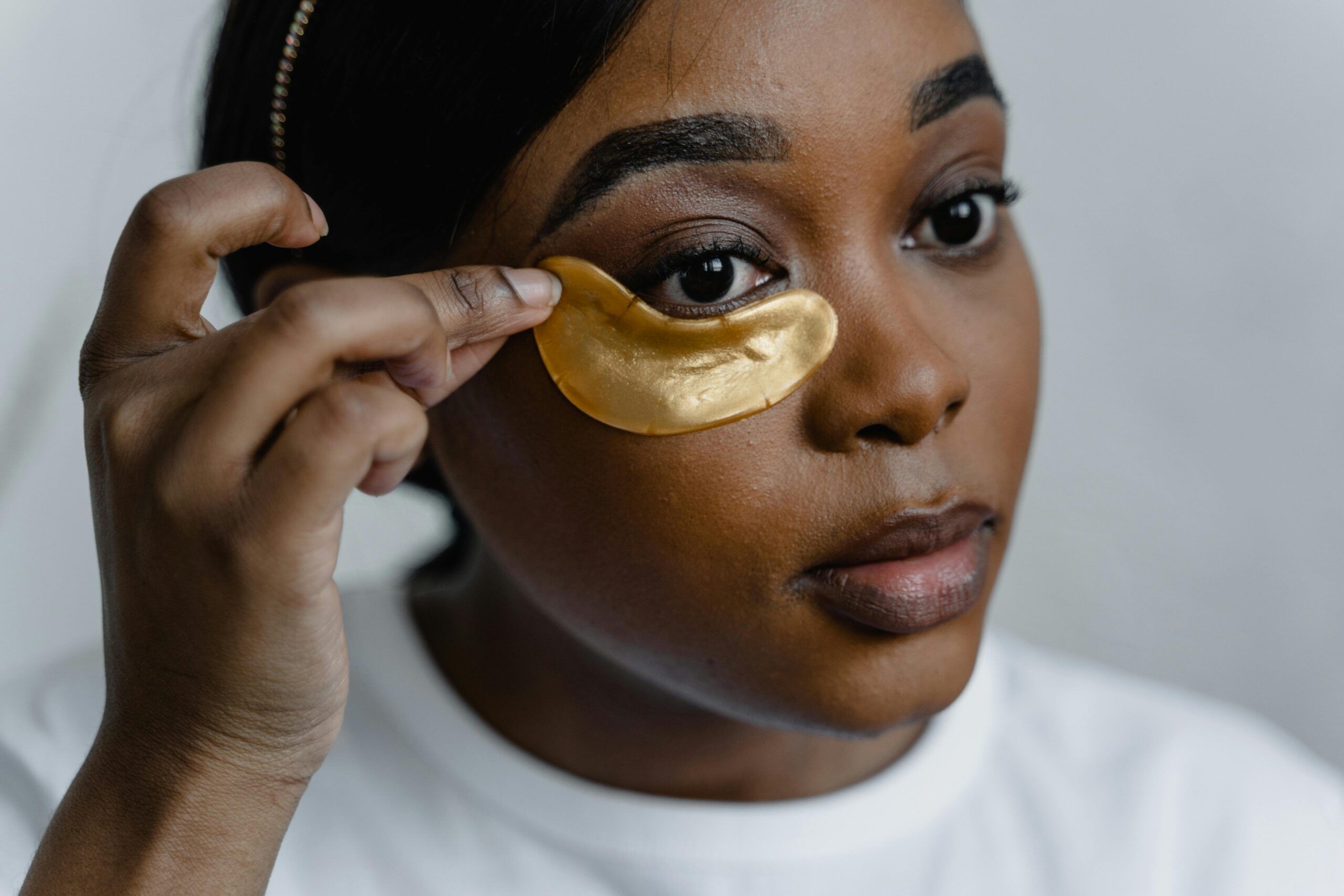Close-up of a woman applying gold eye patches for skincare routine.
